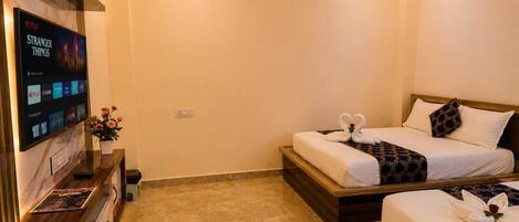 A hotel room with two beds, a TV mounted on the wall, and a small table with a vase of flowers.