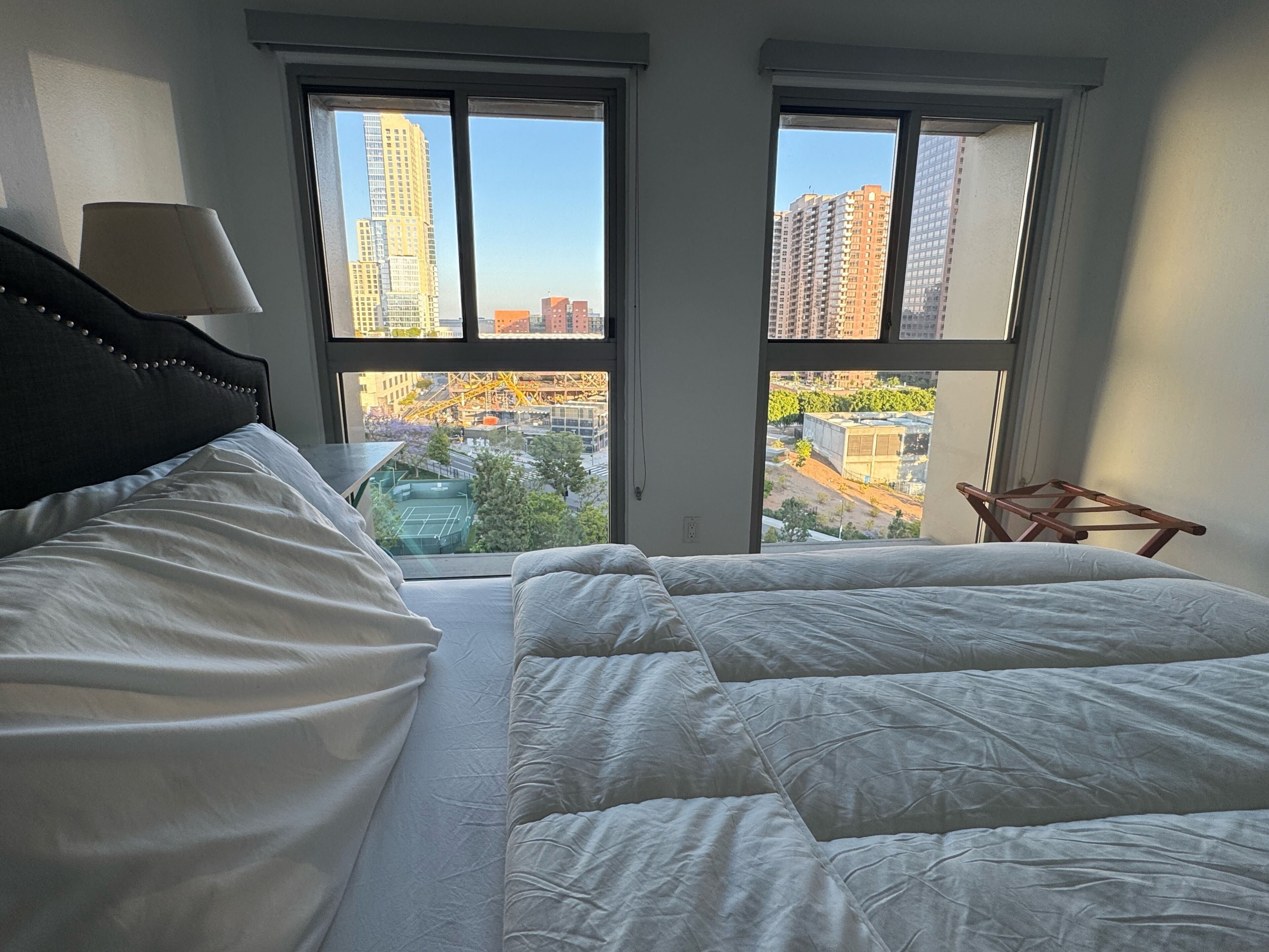Una camera da letto con un letto, una lampada e vista sulla città attraverso due finestre.