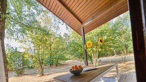 An outdoor wooden table with a bowl of oranges and a vase of sunflowers under a wooden pergola. - Elegant Bungalow With View (Getelo)