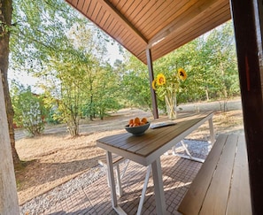 Ein Holztablett im Freien mit einer Orangenschale und einer Vase Sonnenblumen unter einer Holzpergola.