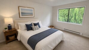 Un dormitorio con cama, mesita de noche, lámpara y ventana con vistas a árboles.