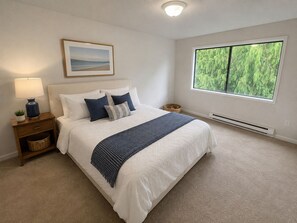 Un dormitorio con cama, mesita de noche, lámpara y ventana con vistas a árboles.