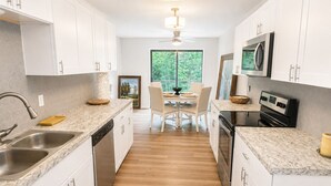 Una cocina moderna con armarios blancos, lavavajillas, estufa y comedor con mesa y sillas.