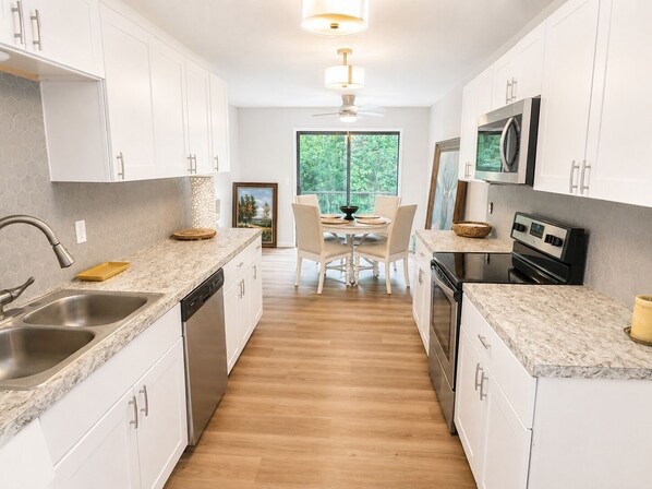 Una cocina moderna con armarios blancos, lavavajillas, estufa y comedor con mesa y sillas.