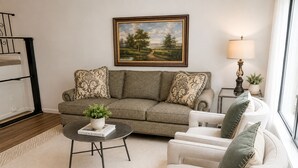 Una sala de estar con sofá, sillón, mesa de centro y un cuadro en la pared.