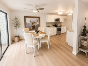 Una cocina moderna con armarios blancos, microondas, horno y un comedor con mesa y sillas.