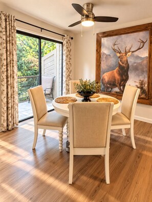 A dining area with a round table, four chairs, a ceiling fan, and a large deer painting on the wall.