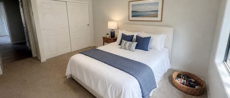 A bedroom with a bed, a nightstand, a lamp, a picture on the wall, a closet, and a window.
