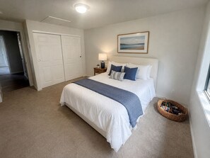 Un dormitorio con cama, mesita de noche, lámpara, cuadro en la pared, armario y ventana.