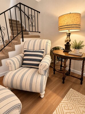 A striped armchair with a cushion, a wooden table with a lamp, and a staircase with black railings.