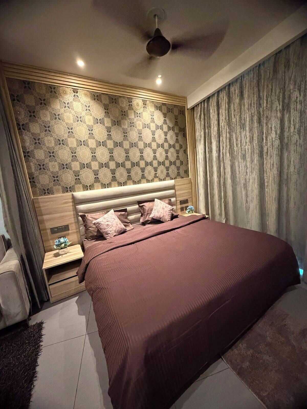 Een slaapkamer met een groot bed, een nachtkastje, een plafondventilator en een behang met een patroon.