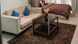 A modern bedroom with a bed, a sofa, a coffee table, and a painting on the wall. - The Spira Skyline Stay (Noida)