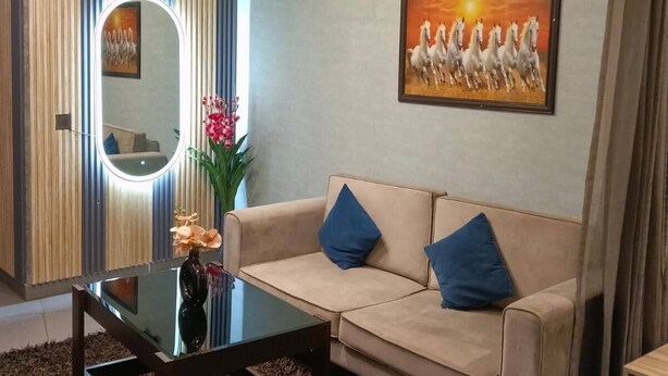 A living room with a sofa, a coffee table, a mirror, a painting of horses, and a decorative light fixture. - The Spira Skyline Stay (Noida)