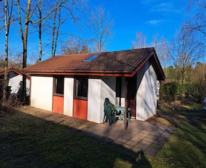 A small, single-story house with a sloped roof, a porch with a table and chairs, and a clear blue sky in the background. - Beautiful Bungalow in Nature (Getelo)