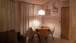 A cozy living room with a round wooden table, four chairs, a sofa, and a large window with curtains. - Beautiful Bungalow in Nature (Getelo)