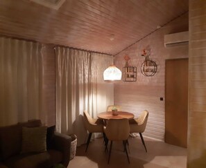 A cozy living room with a round wooden table, four chairs, a sofa, and a large window with curtains. - Beautiful Bungalow in Nature (Getelo)