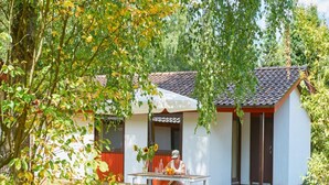 A single-story building with a tiled roof, a small porch, and a table with a person seated. - Beautiful Bungalow in Nature (Getelo)