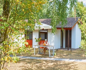 A single-story building with a tiled roof, a small porch, and a table with a person seated. - Beautiful Bungalow in Nature (Getelo)