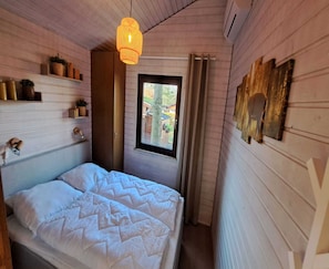 A bedroom with a bed, a hanging light fixture, a window, and wall-mounted decor. - Beautiful Bungalow in Nature (Getelo)