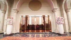 A grand entrance with a reflective glass door, flanked by two large flower vases, leading to a patterned carpet. - La Flora Resort (Meerut)