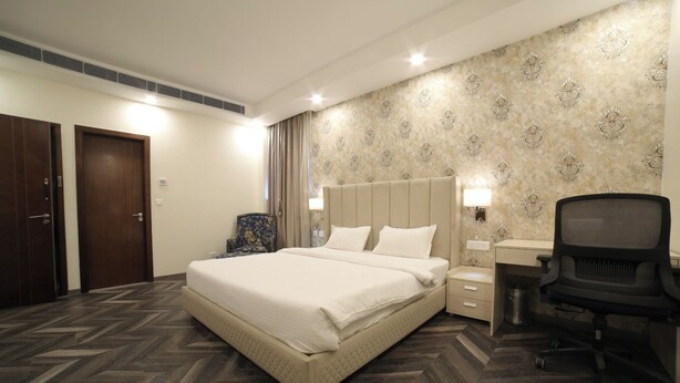 A hotel room with a large bed, a desk with a chair, a wardrobe, and a patterned wall. - La Flora Resort (Meerut)