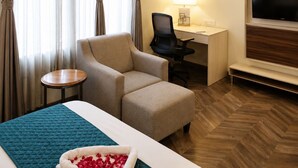 A hotel room with a bed, a desk, a chair, a TV, and a painting on the wall. - La Flora Resort (Meerut)