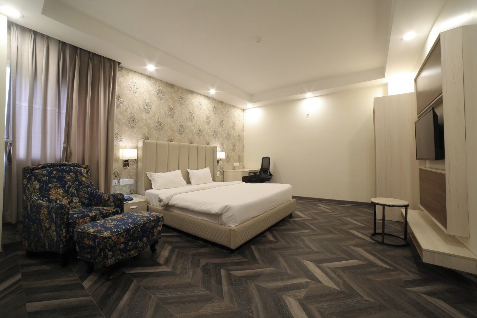 Een hotelkamer met een bed, een stoel, een bureau, een televisie en een kamer met een patroon op de muur.