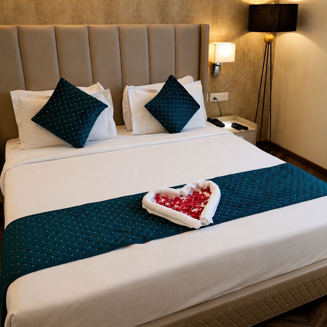 Habitación de hotel con cama, almohadas, mesita de noche con lámpara y televisión montada en la pared.