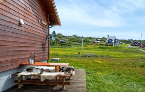 Un bâtiment en bois doté d’une terrasse et de bancs, d’une antenne parabolique, et offrant une vue sur un paysage verdoyant avec des maisons visibles au loin.