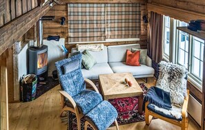 Ein gemütliches Blockhaus-Interieur mit einer Couch, zwei Sesseln, einem Tisch, einem Kamin und einem Fenster.