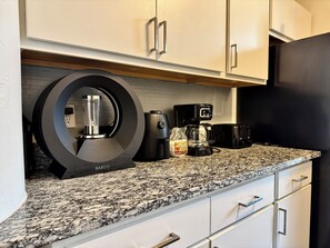 A kitchen with a granite countertop, a coffee maker, a blender, and a refrigerator. - Modern Downtown Indianapolis Condo (Indianapolis)