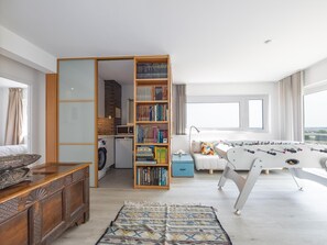 A well-lit room with a wooden bookshelf, a washing machine, a sofa, and a foosball table. - Three-bedroom apartment with sea view (Middelkerke)