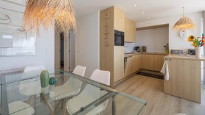 A modern kitchen with wooden cabinets, a glass dining table, and a hanging light fixture. - Three-bedroom apartment with sea view (Middelkerke)