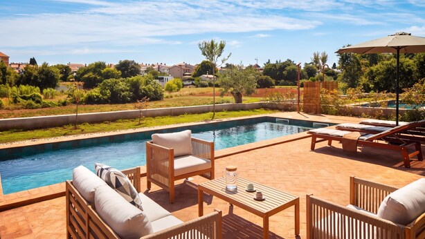 Piscina com espreguiçadeiras e uma mesa, cercada por um terraço de tijolos.