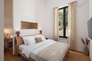 Ein Schlafzimmer mit Bett, Nachttischen, einem Fenster mit Vorhängen, einem an der Wand befestigten Fernseher und einer Vase mit Trockenpflanzen.