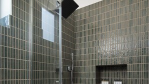 Uma casa de banho moderna com área de duche, paredes em azulejo e um armário embutido com artigos de higiene pessoal.