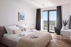 Habitación de hotel moderna con una cama grande, un escritorio, una silla, una planta en maceta y vistas a la ciudad.