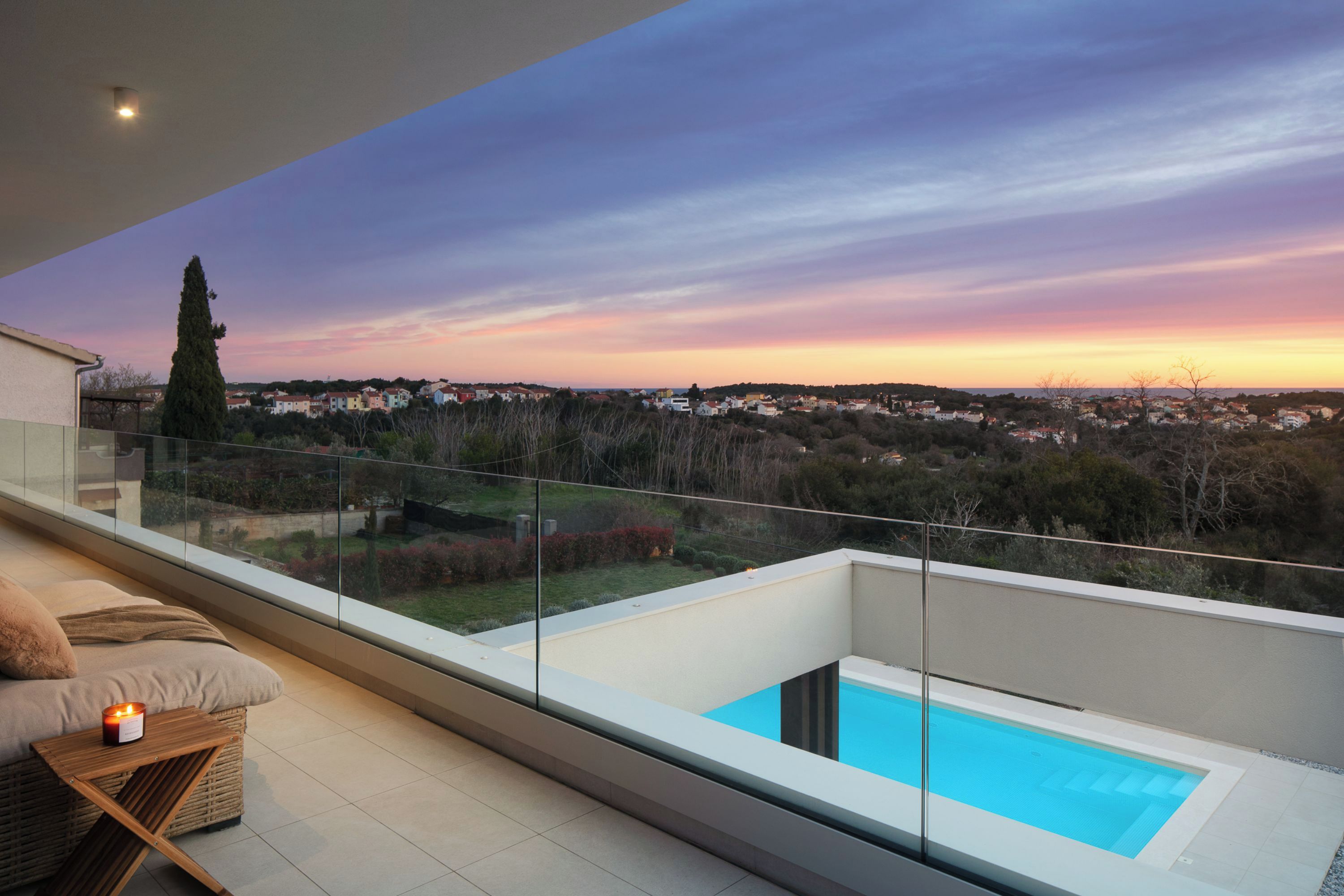 Ein Balkon mit Glastrennung, der einen Blick auf einen Pool und einen Sonnenuntergang bietet.