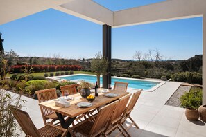 Eine sonnendurchflutete Terrasse mit Pool, Holzmöbeln und freiem Blick auf die umliegende Landschaft.