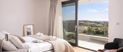 A bedroom with a bed, a chair, a window with a view, and a door.