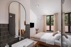 A hotel room with a large mirror, a bedside table, a bed with pillows, a window with curtains, and a view of greenery outside. - Case Atrio Villas (Rovinj)