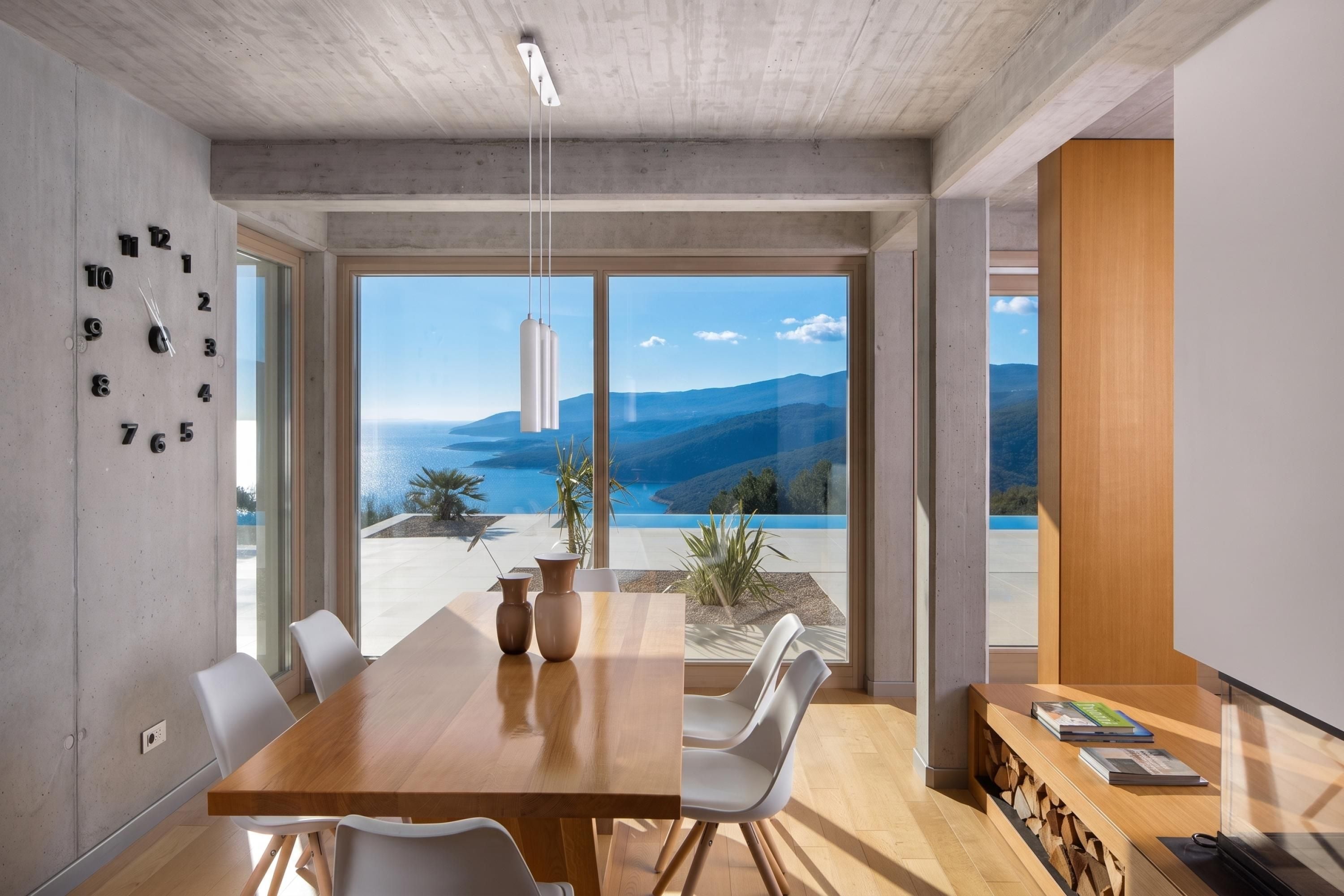 A modern dining area with a wooden table, white chairs, and a view of a mountainous landscape through large windows.