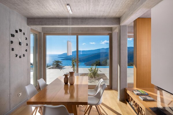 Un comedor moderno con una mesa de madera, sillas blancas y vistas a un paisaje montañoso a través de amplios ventanales.