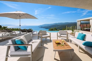 A terrace with white furniture, a wooden table with a bowl of lemons, and a view of the sea and mountains. - Villa Mayan Luxury Sea View Retreat With Pool & Sauna (Labin)