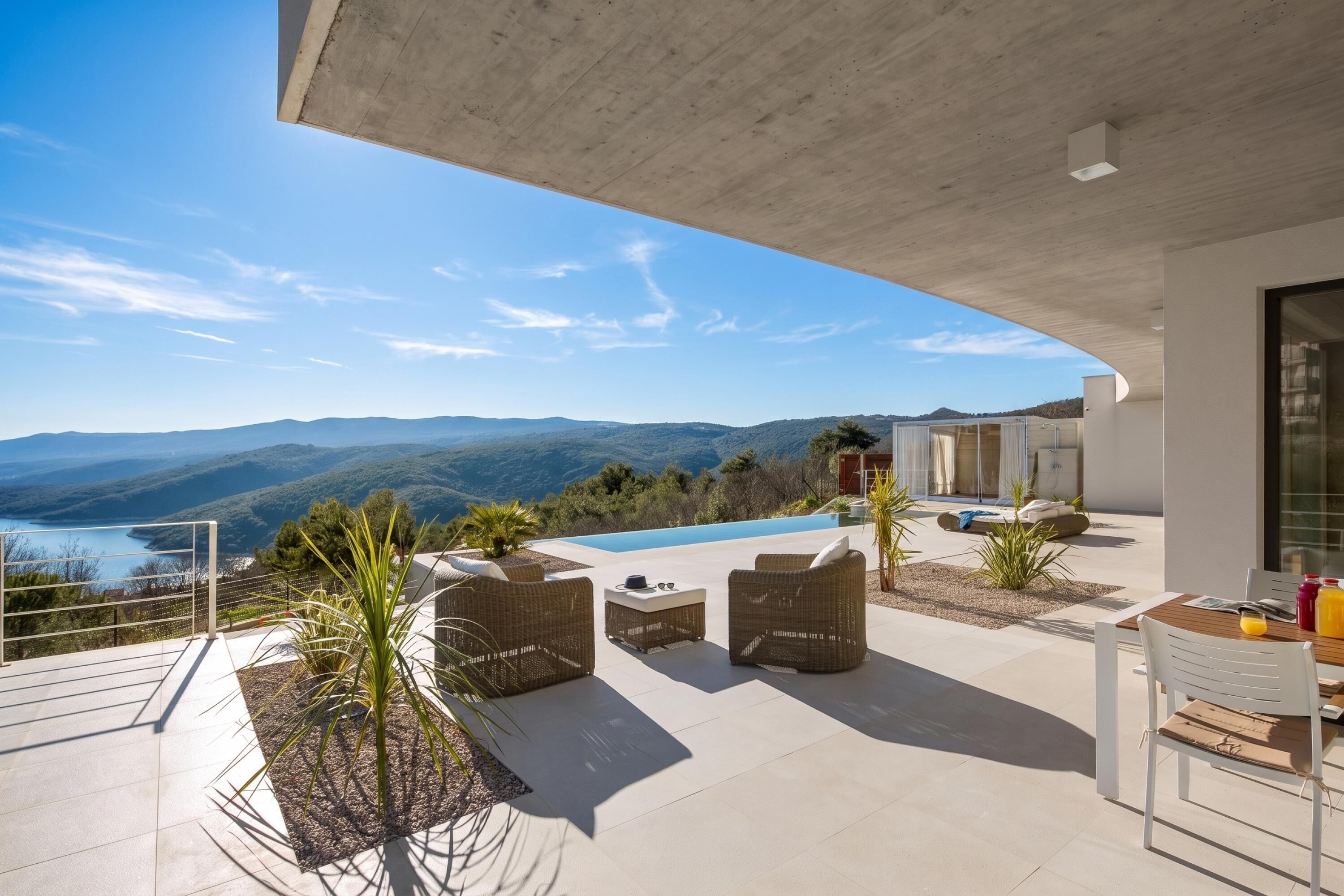 A modern outdoor terrace with a pool, wicker furniture, and a view of the mountains.