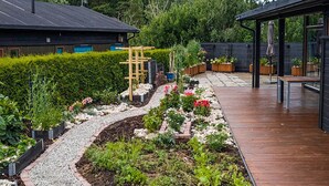 Ein Garten mit Kiesweg, verschiedenen Pflanzen, einem Holzsteg und einer Holzterrasse.