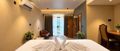 A hotel room with a bed, a desk, a chair, a dining table, and a view of the outdoors.
