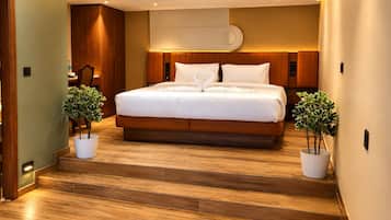Quarto de hotel moderno com uma cama grande, piso de madeira e duas plantas em vasos.
