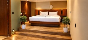A modern hotel room with a large bed, wooden flooring, and two potted plants. - AURA 42 BY DIMORA (Devikolam)