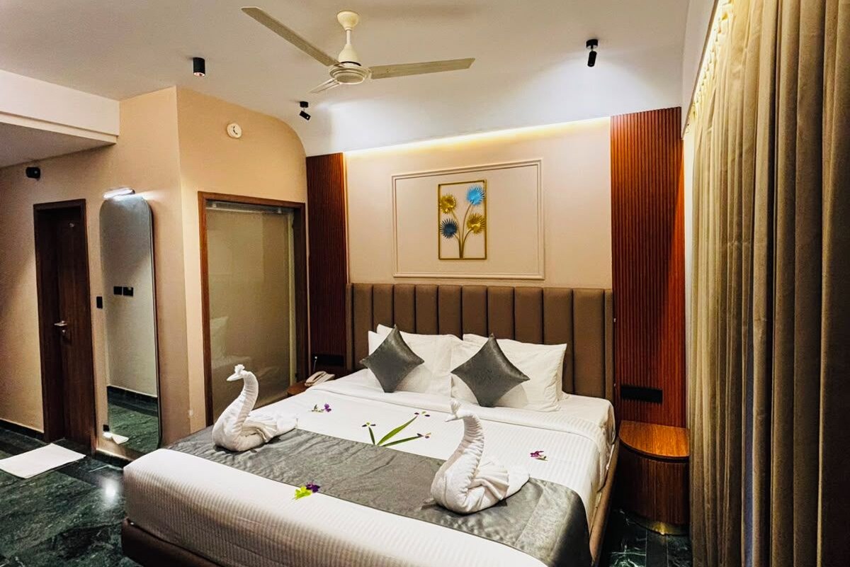 Una habitación de hotel con cama, ventilador de techo, espejo, puerta y cortina.